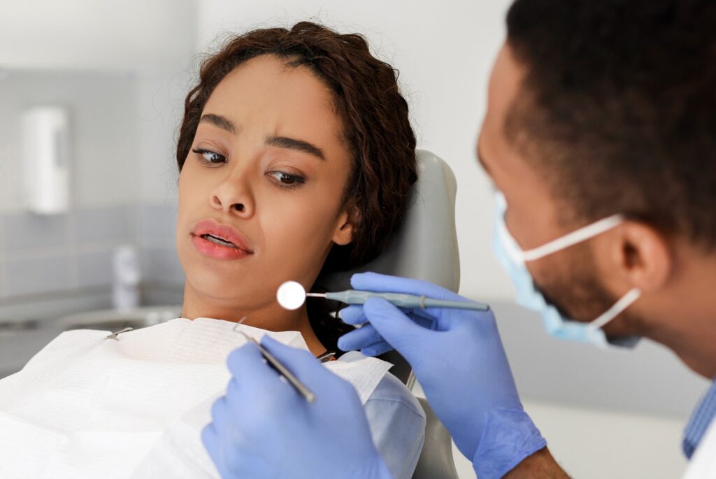 Scared black woman looking at dental tools in doctor hands